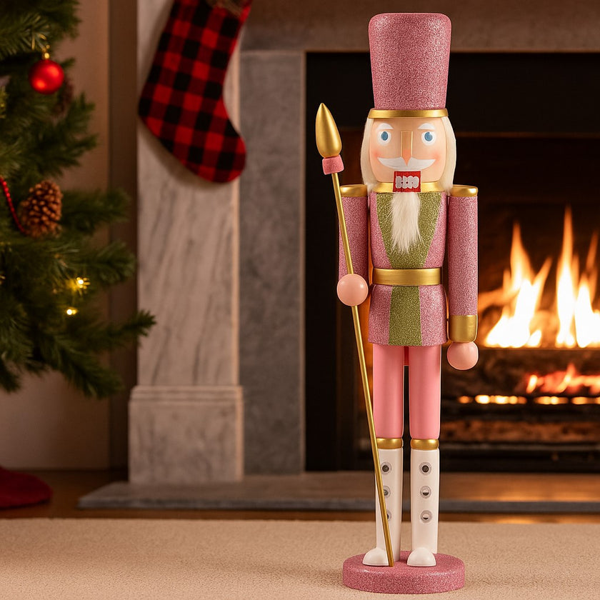 Spărgător de nuci roz cu sclipici și sceptru auriu așezat în fața unui șemineu ce arde