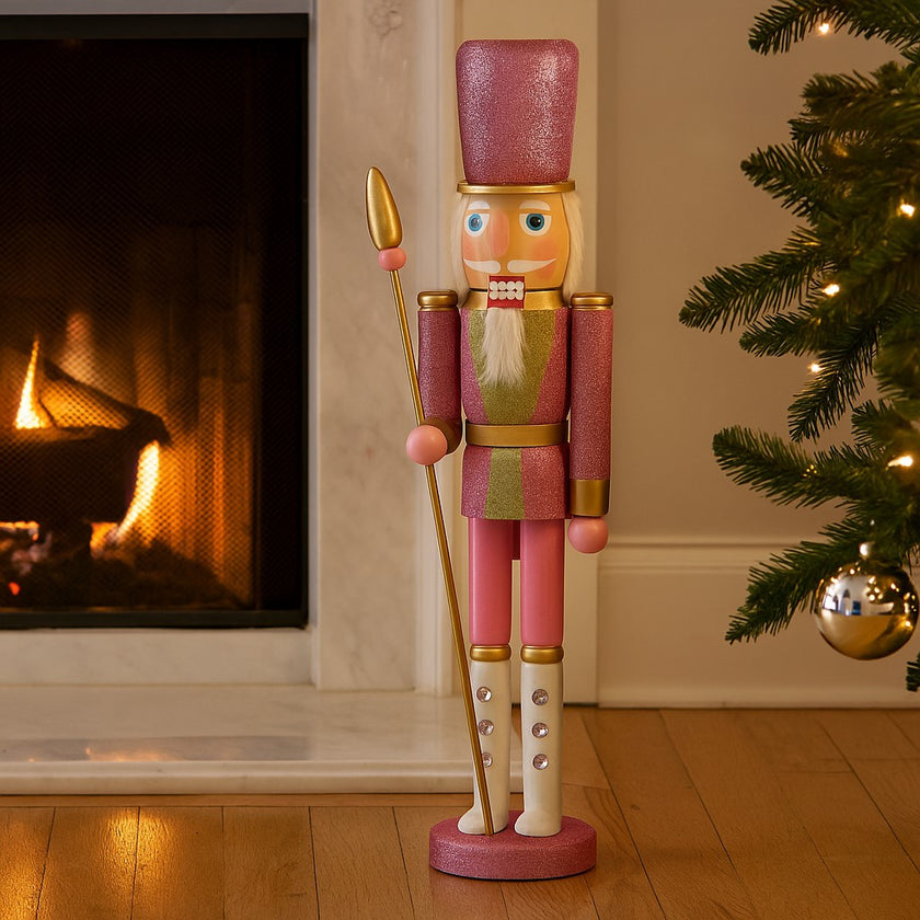 Spărgător de nuci roz cu sclipici și sceptru auriu așezat lângă un șemineu