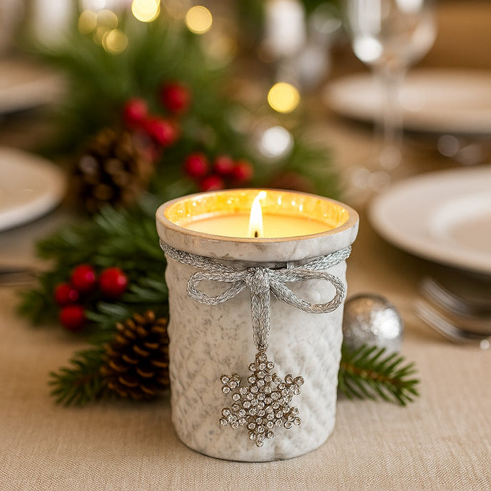 Suport de lumânare din sticlă albă, aprins, pe o masă decorată de Crăciun cu ramuri de brad