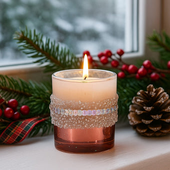 Suport de lumânare din sticlă roz, cu paiete, aprins, pe un pervaz decorat de Crăciun