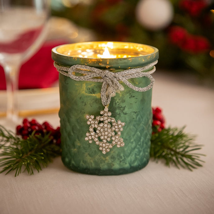 Suport de lumânare din sticlă verde, aprins, pe o masă decorată de Crăciun