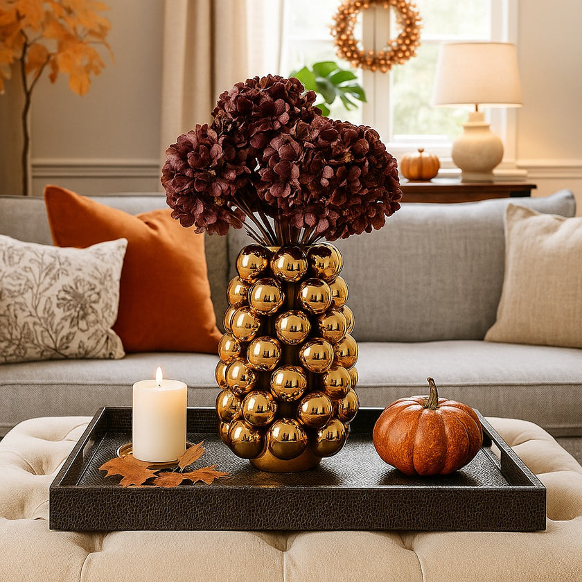 Vază decorativă auriu lucios, cu model în formă de bubble și un buchet de flori în ea, așezată pe o tavă de piele, decorată de toamnă