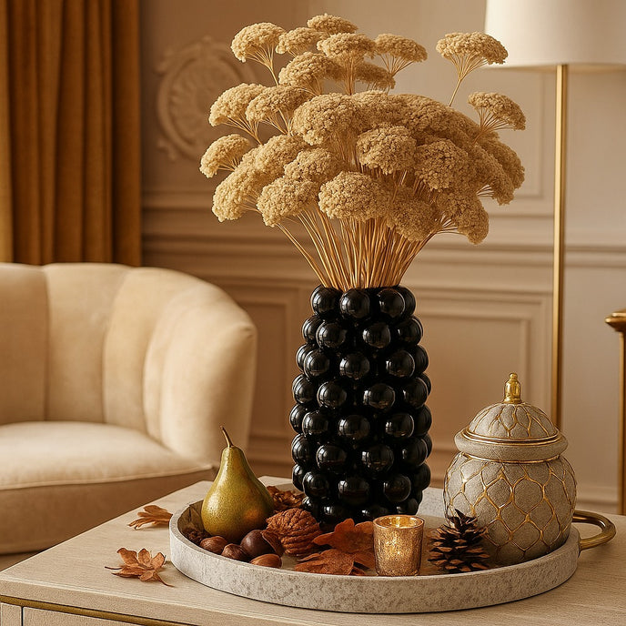 Vază decorativă negru lucios, cu model în formă de bubble și un buchet de flori în ea, așezată pe o tavă rotundă, de piatră, decorată de toamnă