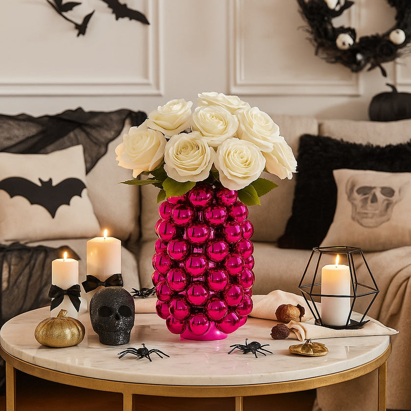 Vază decorativă roz lucios, cu model în formă de bubble și un buchet de flori în ea, așezată pe o masă rotundă, aurie, cu blat de marmură, decorată de Halloween